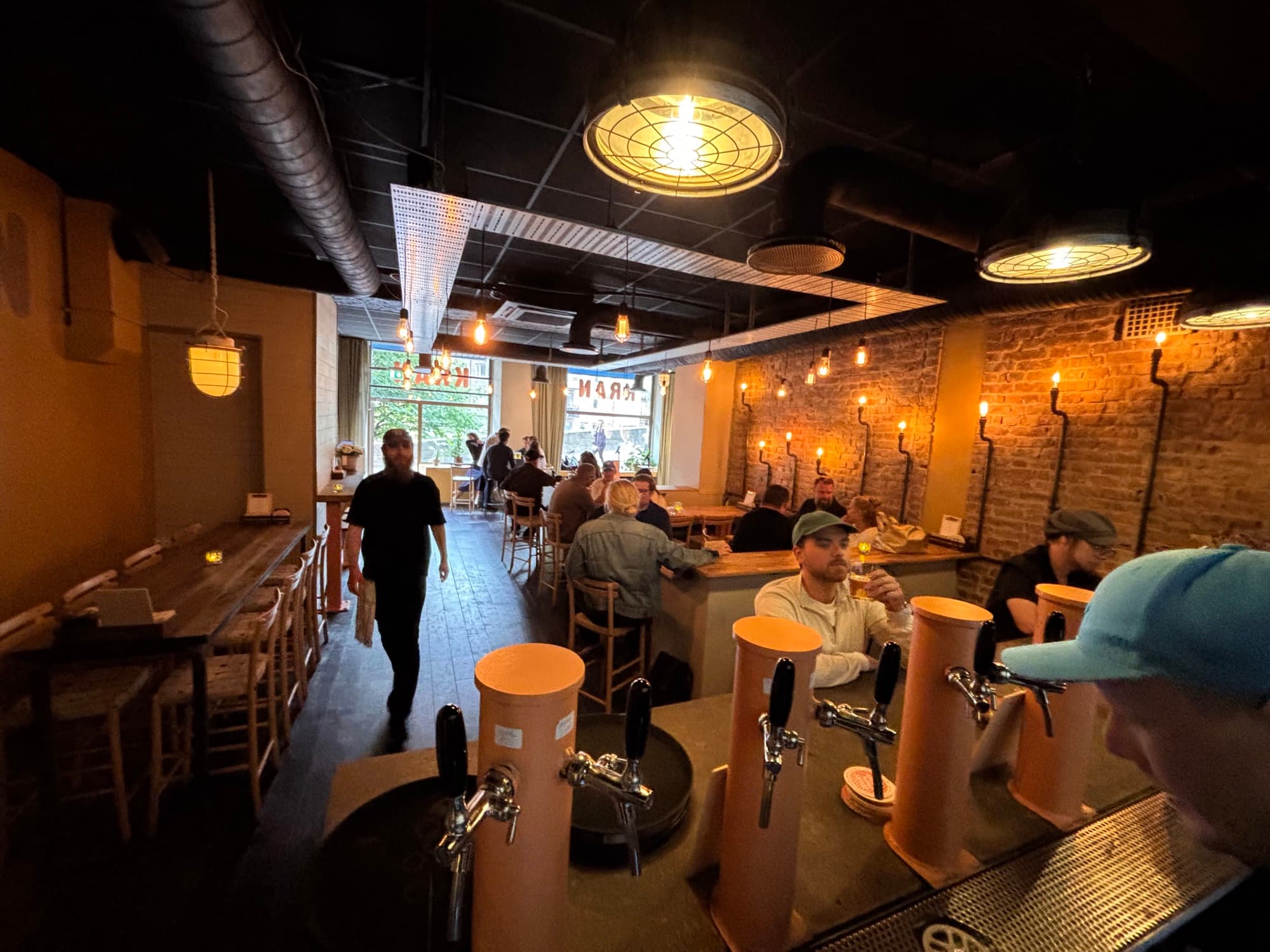 The bar at Kran with its brick wall, warm lamps and guests along the counter