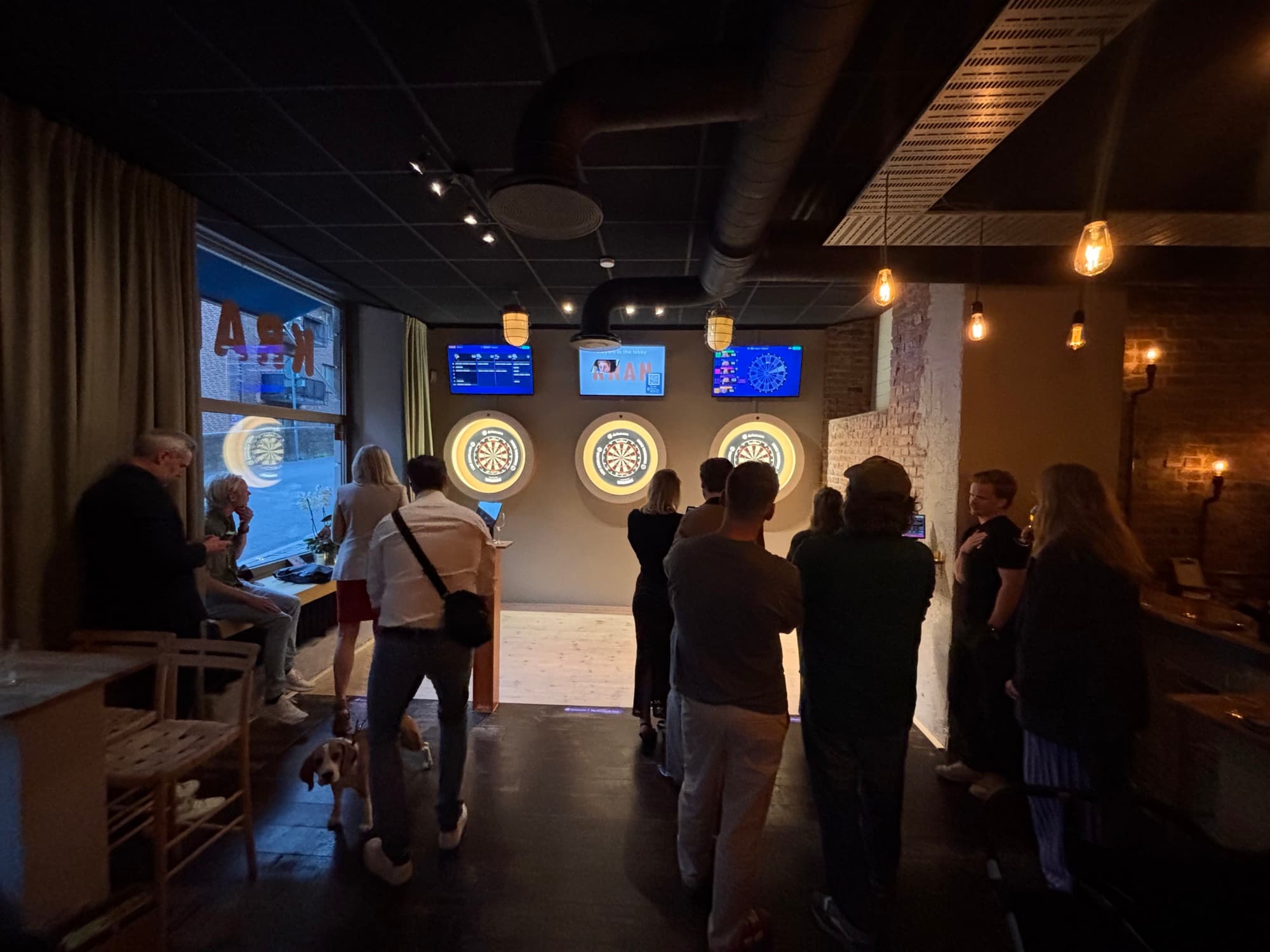 Guests playing darts in the darts room at Kran, in front of three lit dartboards with scoring screens above