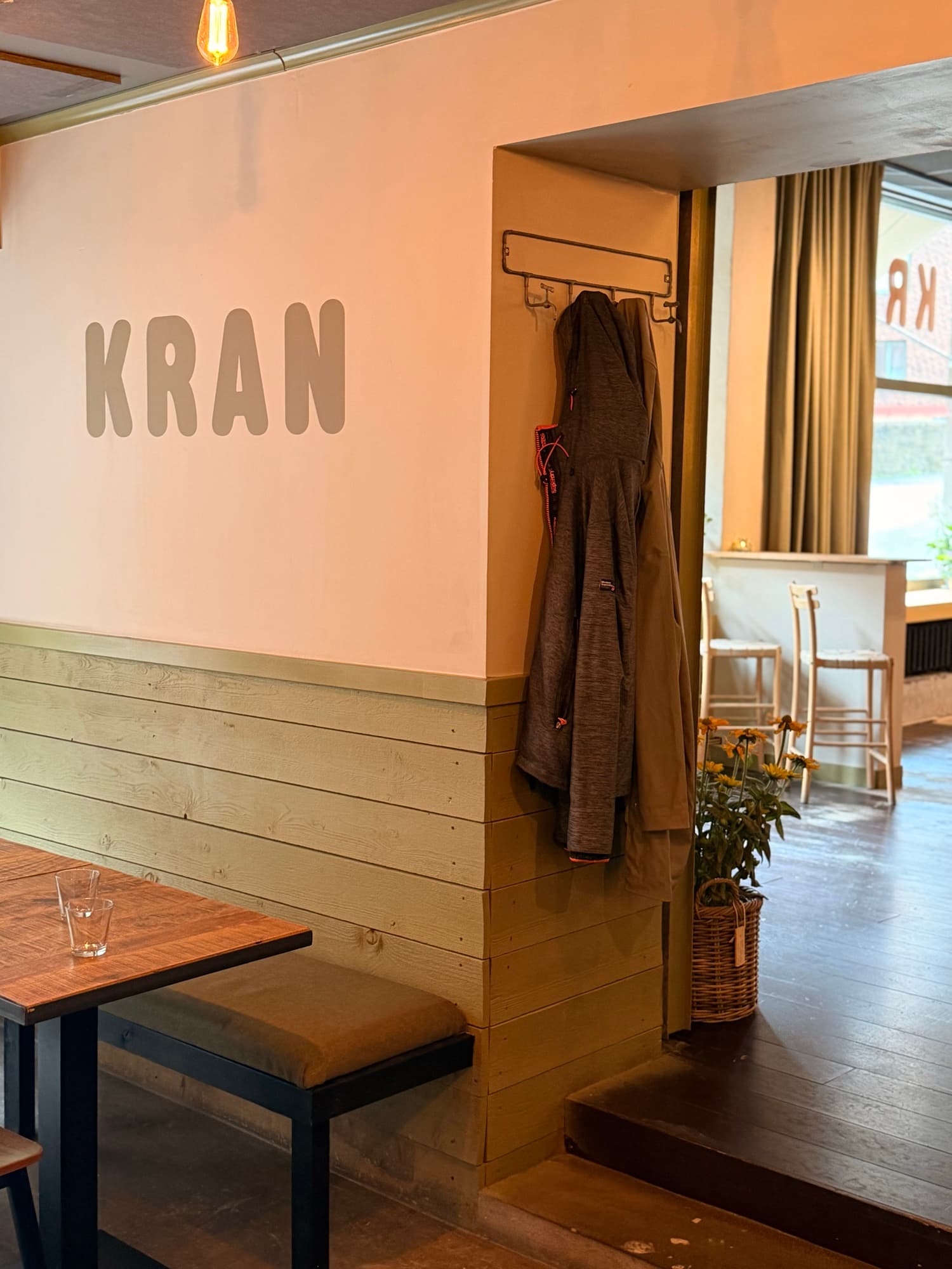 KRAN painted on the wall above the bench seating, with a coat rack and olive wood panelling